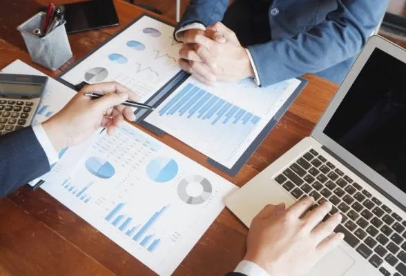Foto de una mesa con documentos de dos hombres de negocios conversando sobre consultoría empresarial